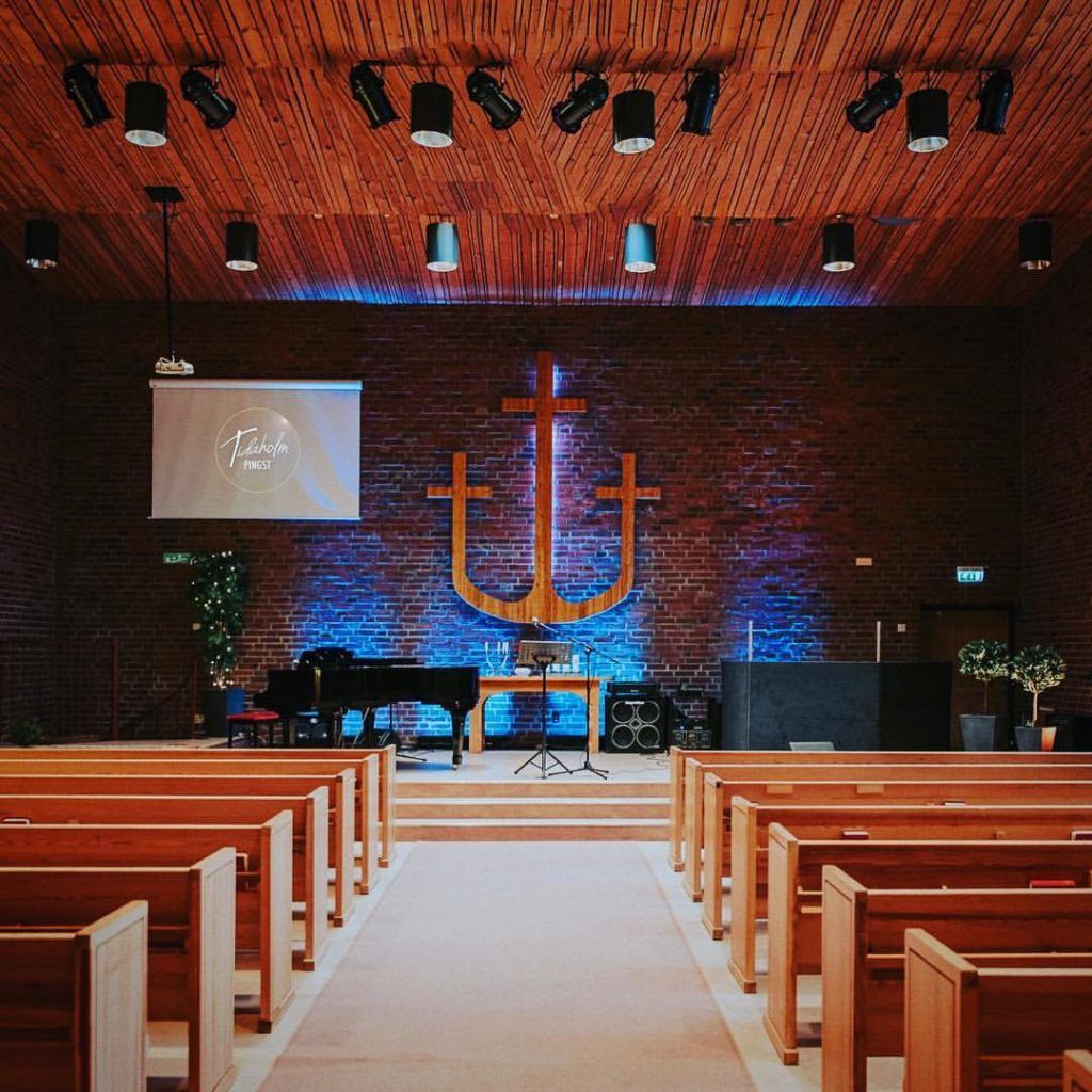 Kyrksalen i Pingstkyrkan i Tidaholm, med korset och ankaret på tegelväggen i blått ljus